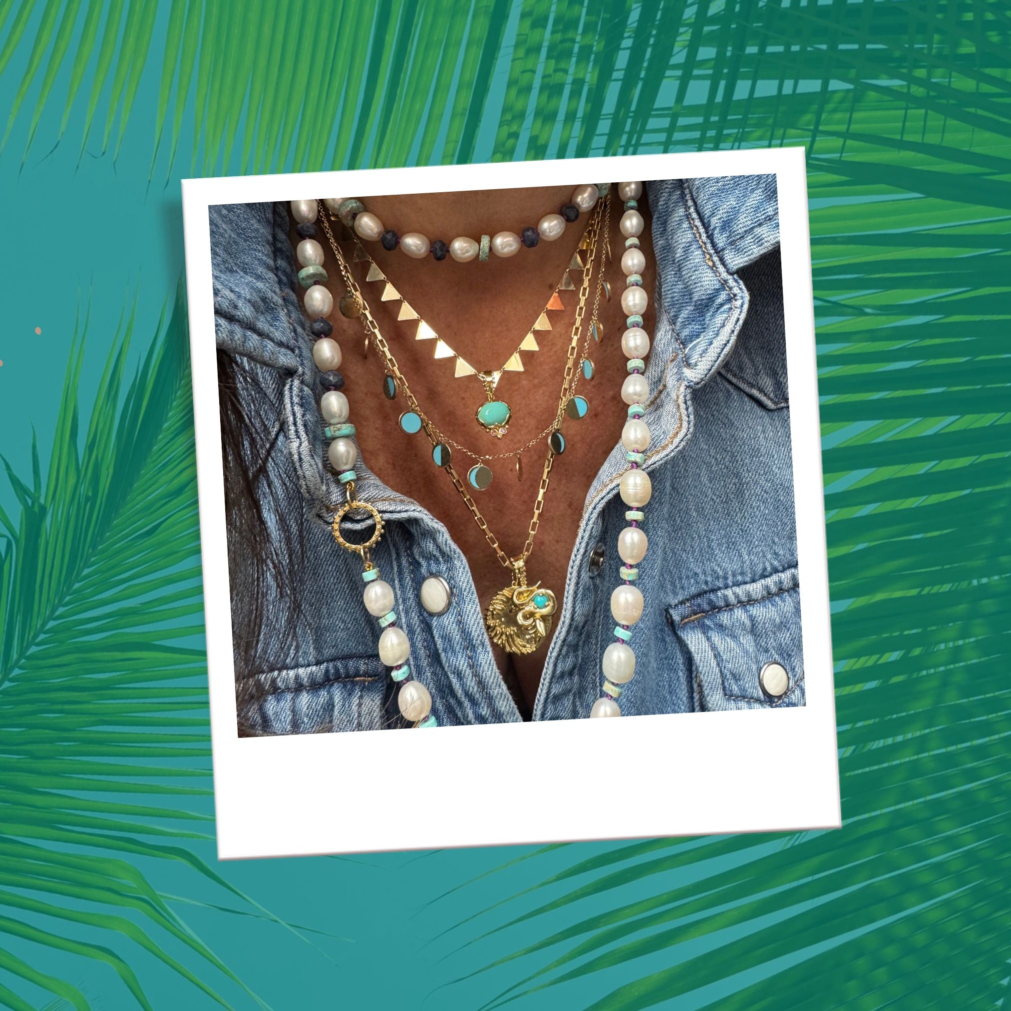 Layered gold talismans with turquoise moon phases and lion pendant, styled with pearls and denim over a teal palms background