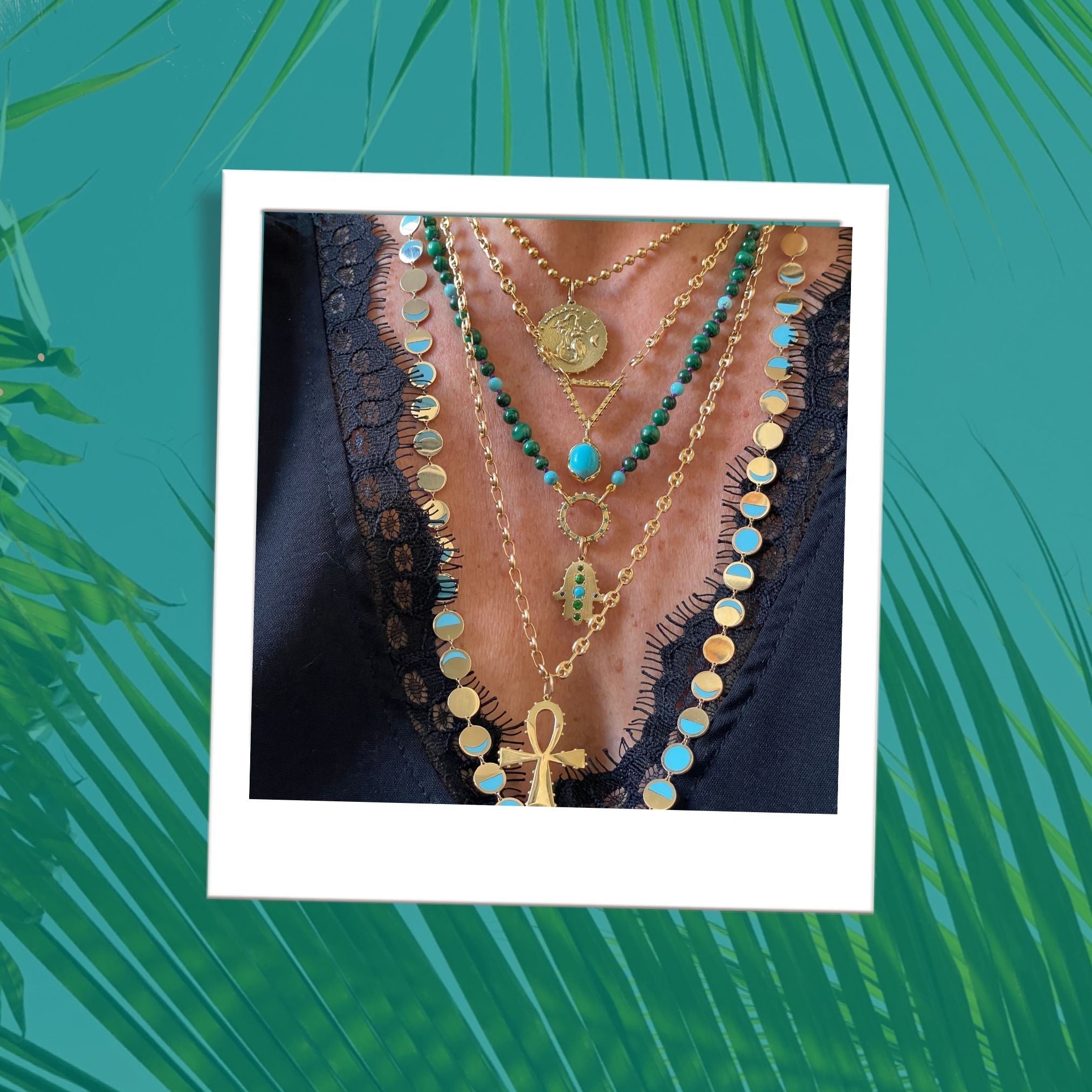 Delphine Leymarie spiritual fine jewelry layered solid gold talisman necklaces with turquoise and green gems, worn with black lace top.