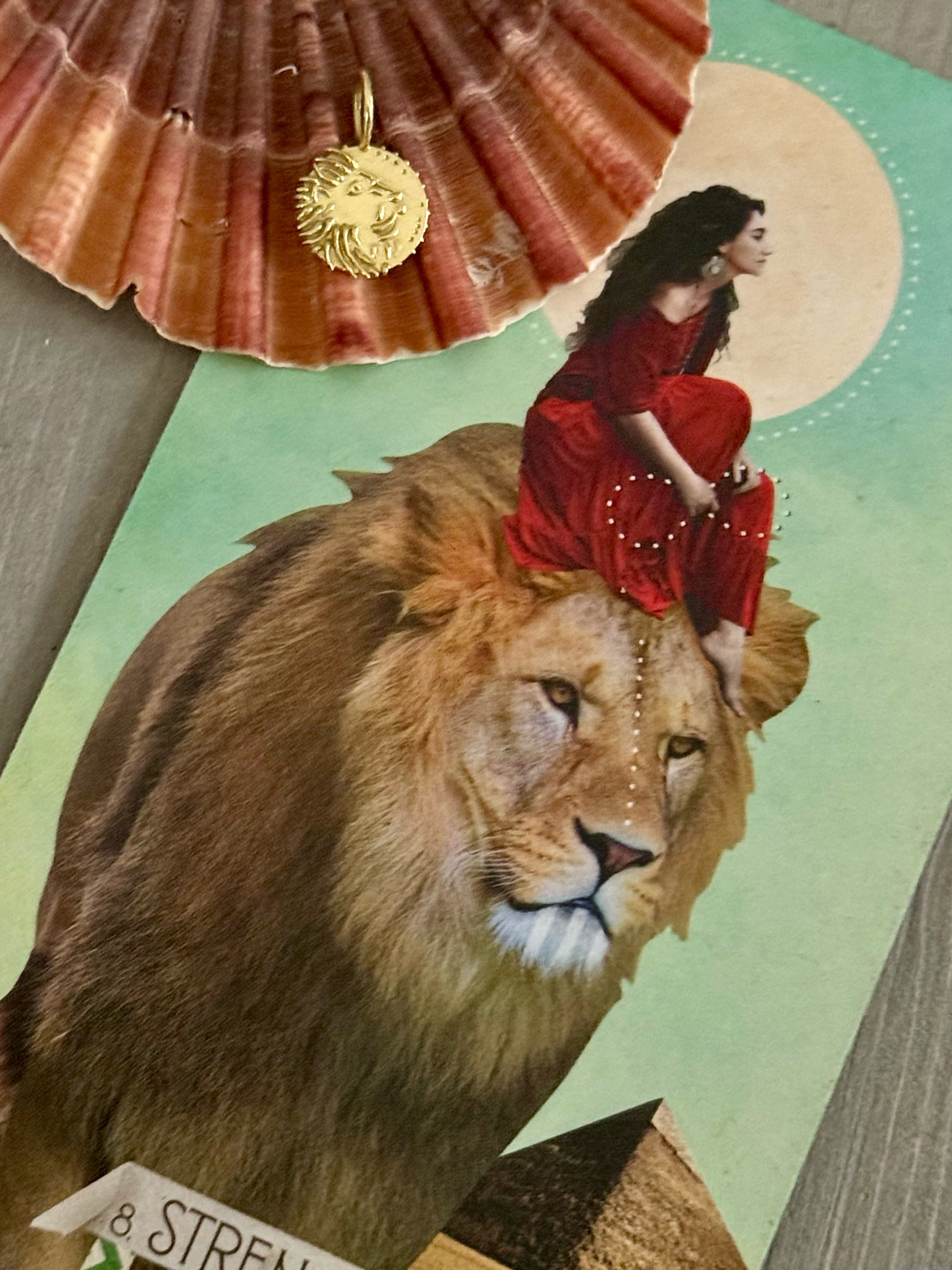 Petit Lion solid 18k recycled gold talisman resting on the Strength tarot card, showing a woman seated on a lion, symbolizing courage, inner power and self-mastery.