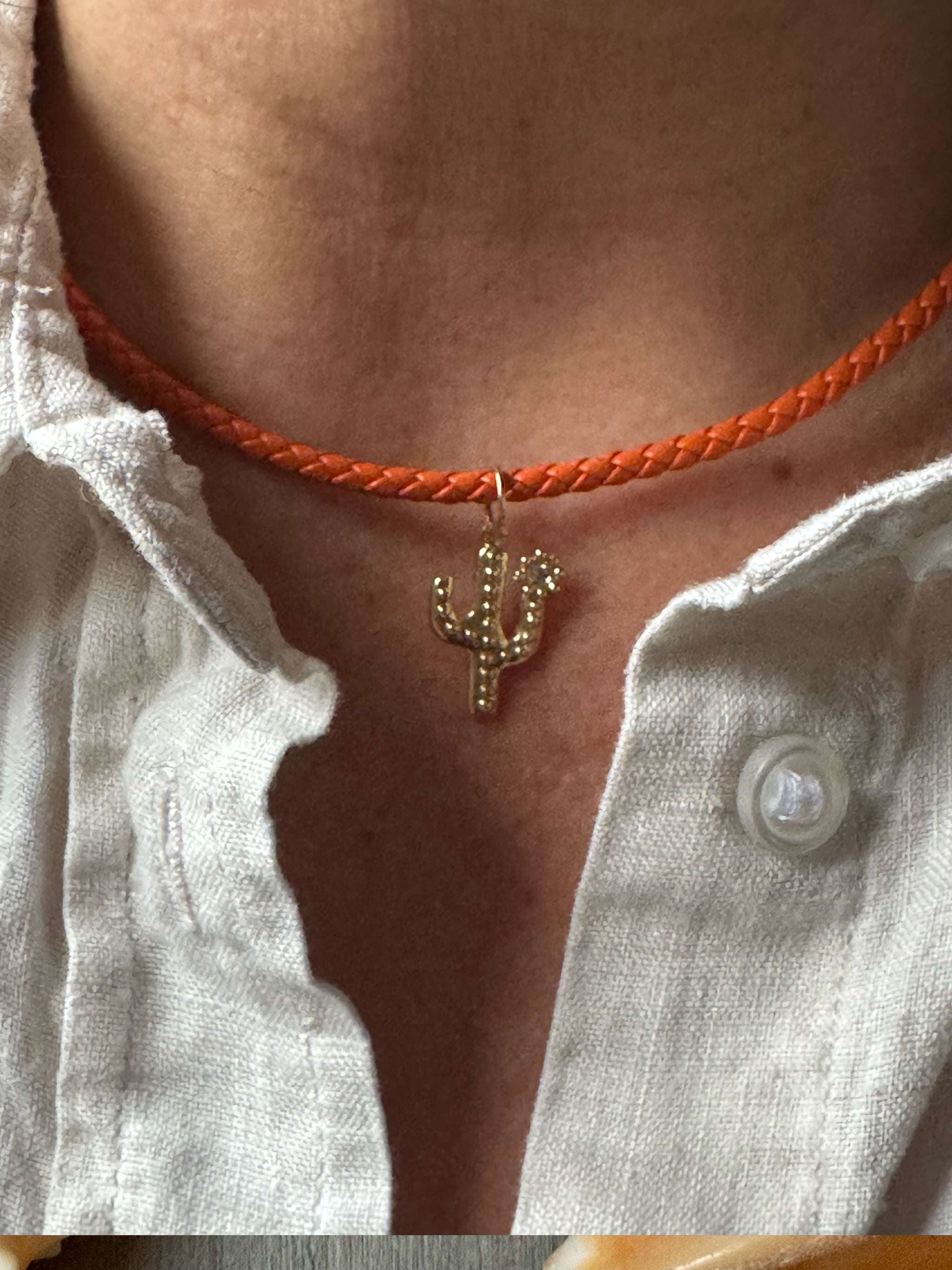 Person wearing the Sacred Link braided orange cord necklace with a cactus pendant on a white linen shirt.