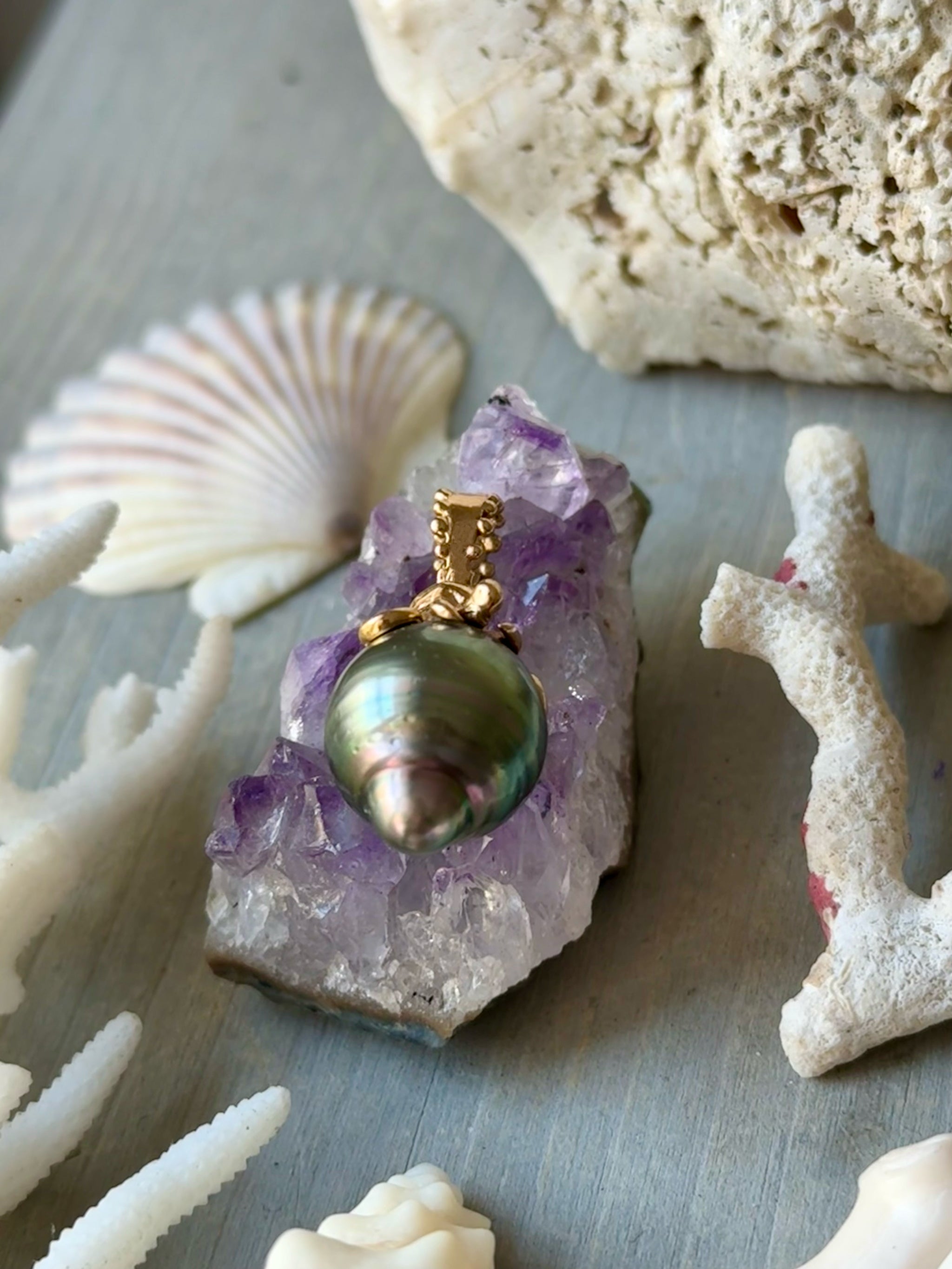 Close-up of Delphine Leymarie Boheme octopus and Tahitian Pearl Talisman in 18k rose goldan amethyst crystal with shells and coral in the background