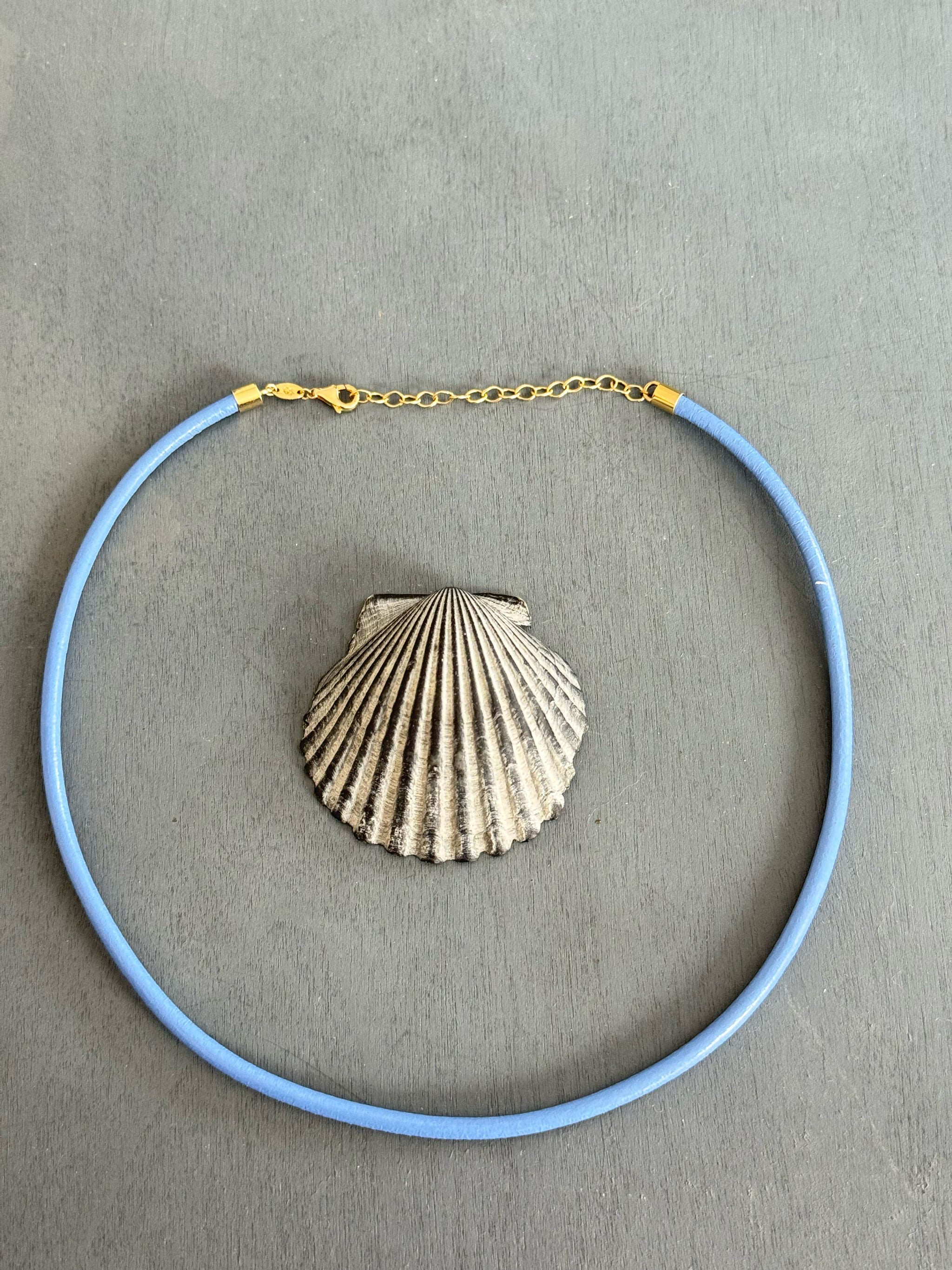 Sacred Link periwinkle blue leather cord with solid 14k yellow gold clasp and extender around a grey shell