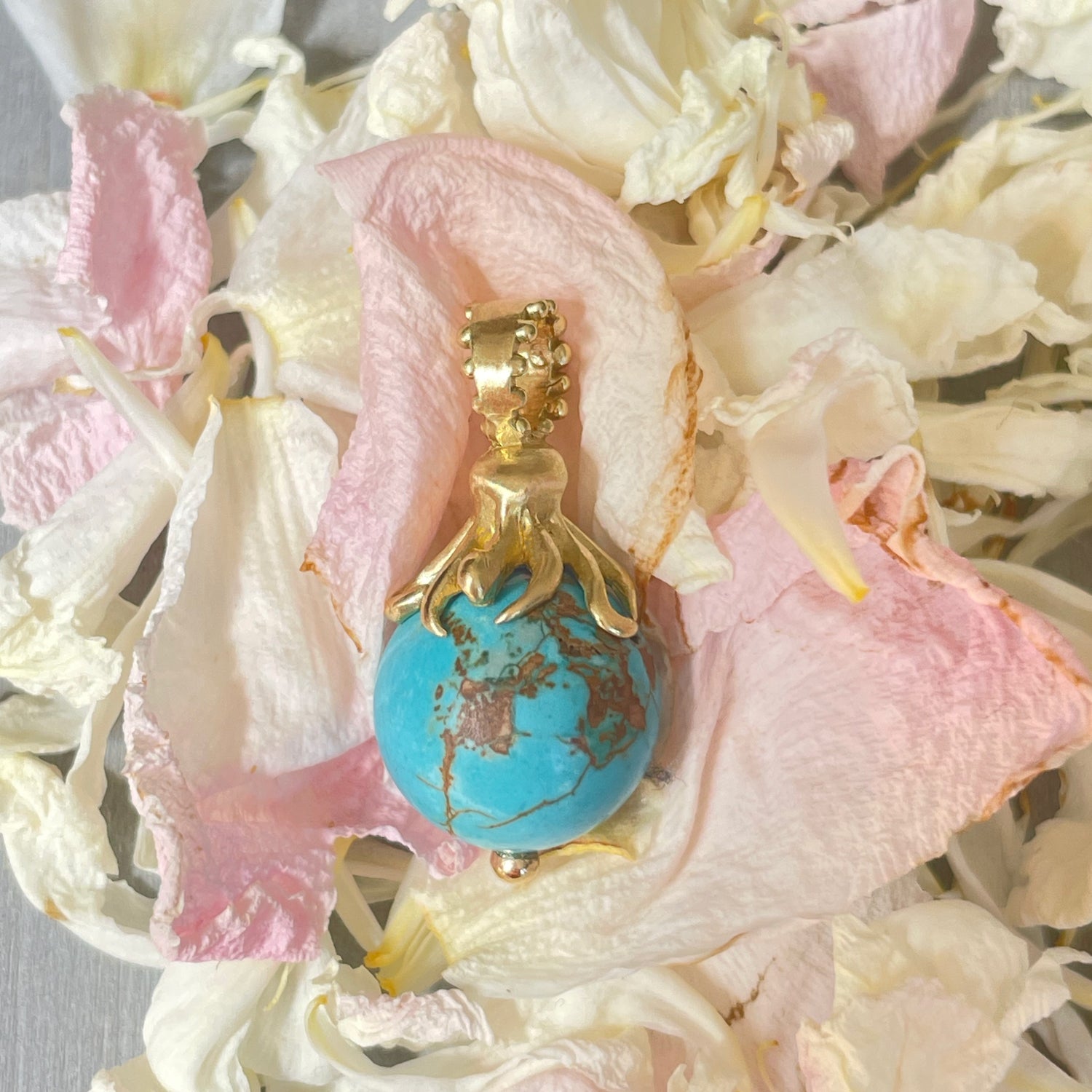 A Delphine Leymarie 18k yellow gold octopus charm capping a turquoise bead, placed on a dried rose petals.