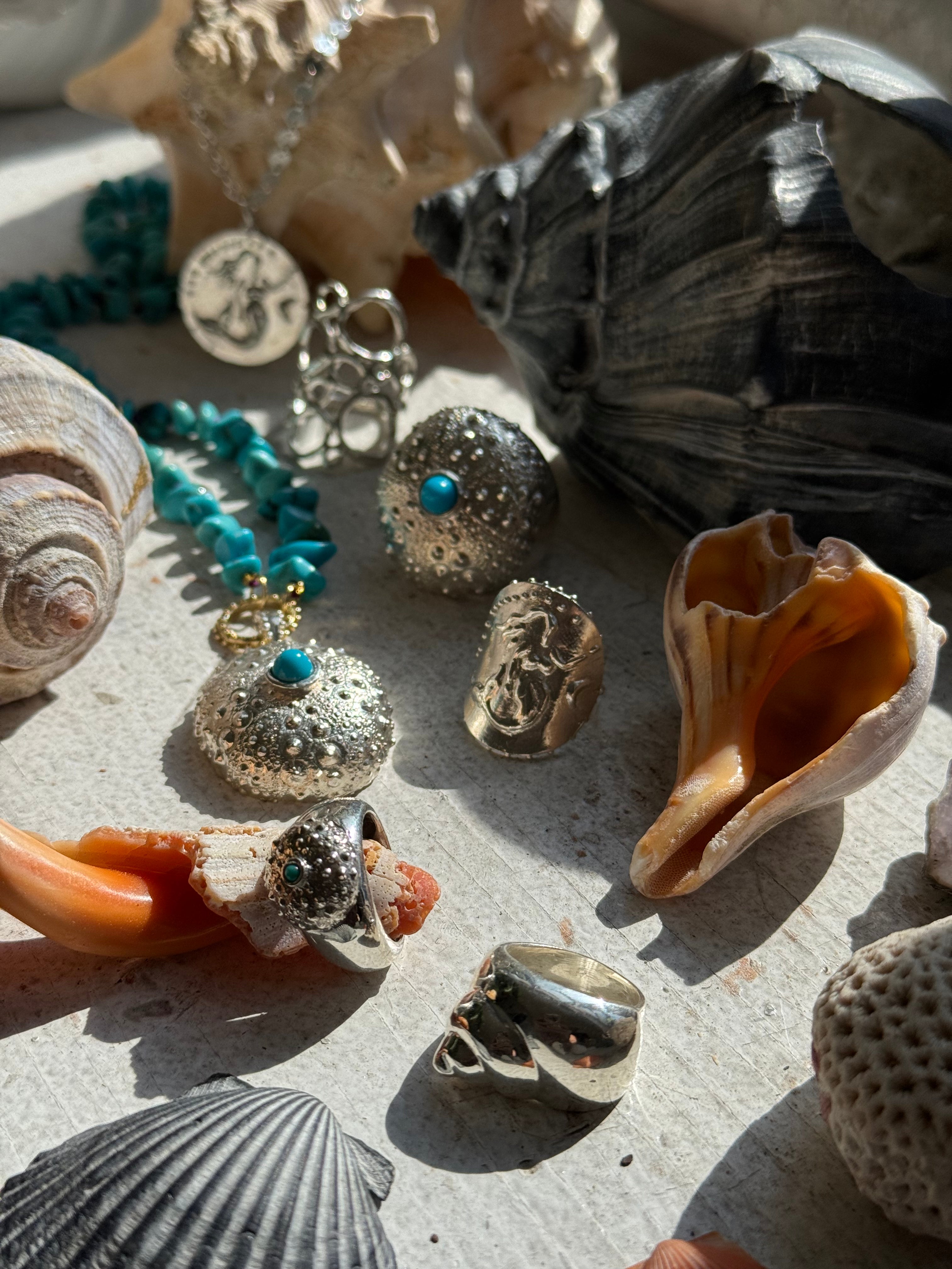 Sunny flatlay of the beach-inspired SeaSpell turquoise and silver jewels surrounded by natural seashells