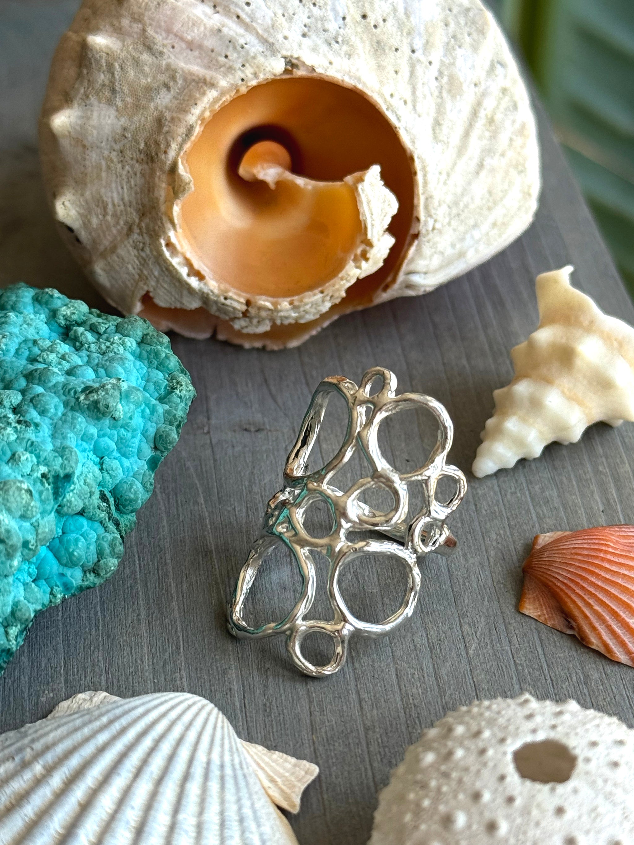 Ecume Ring shown beside ocean Shells, capturing the movement of Sea Foam in sculpted silver.