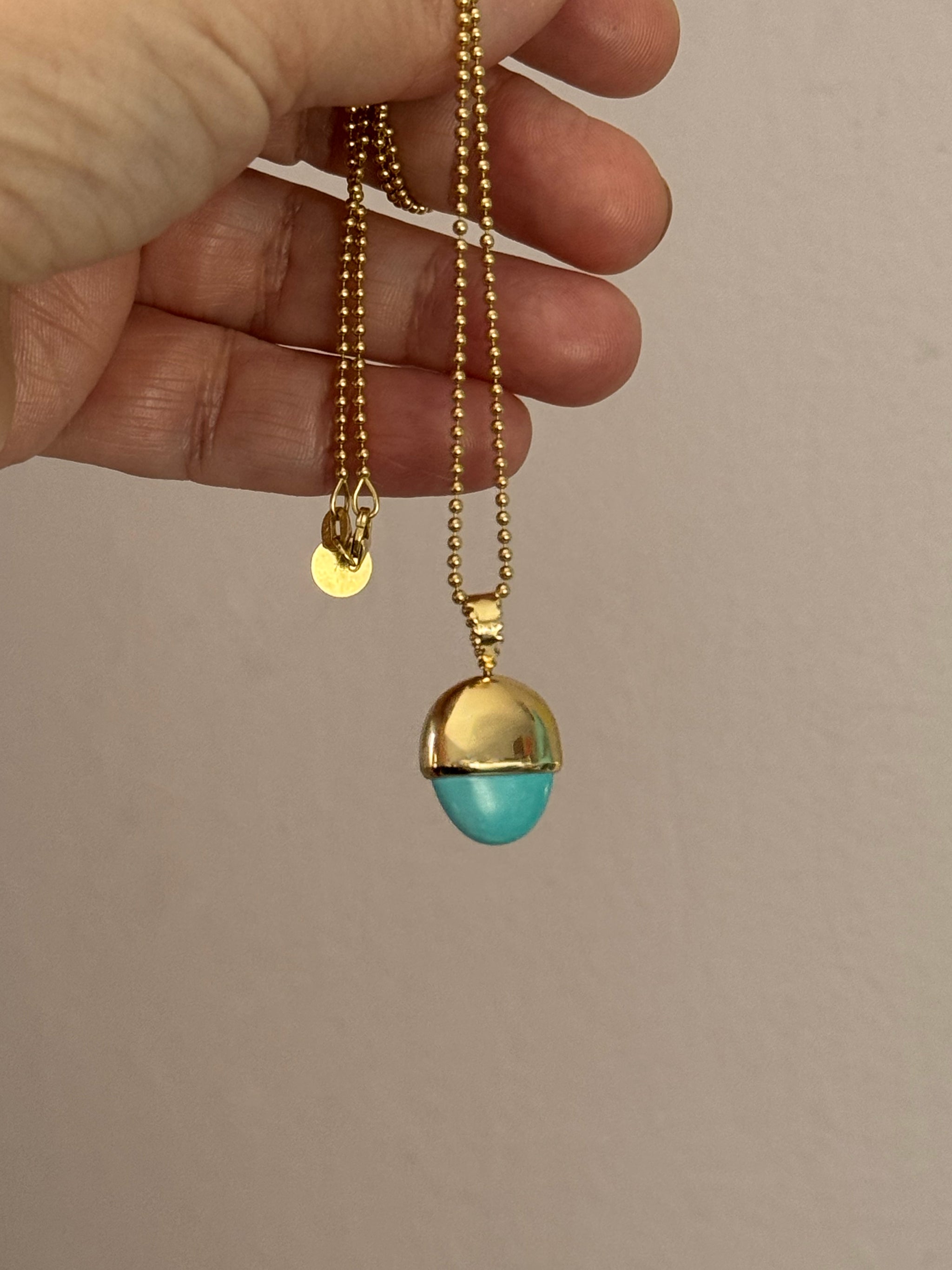 SeaSpell Le Pendule pendulum charm in solid 18k recycled gold with Sleeping Beauty turquoise on gold ball chain, held in hand.