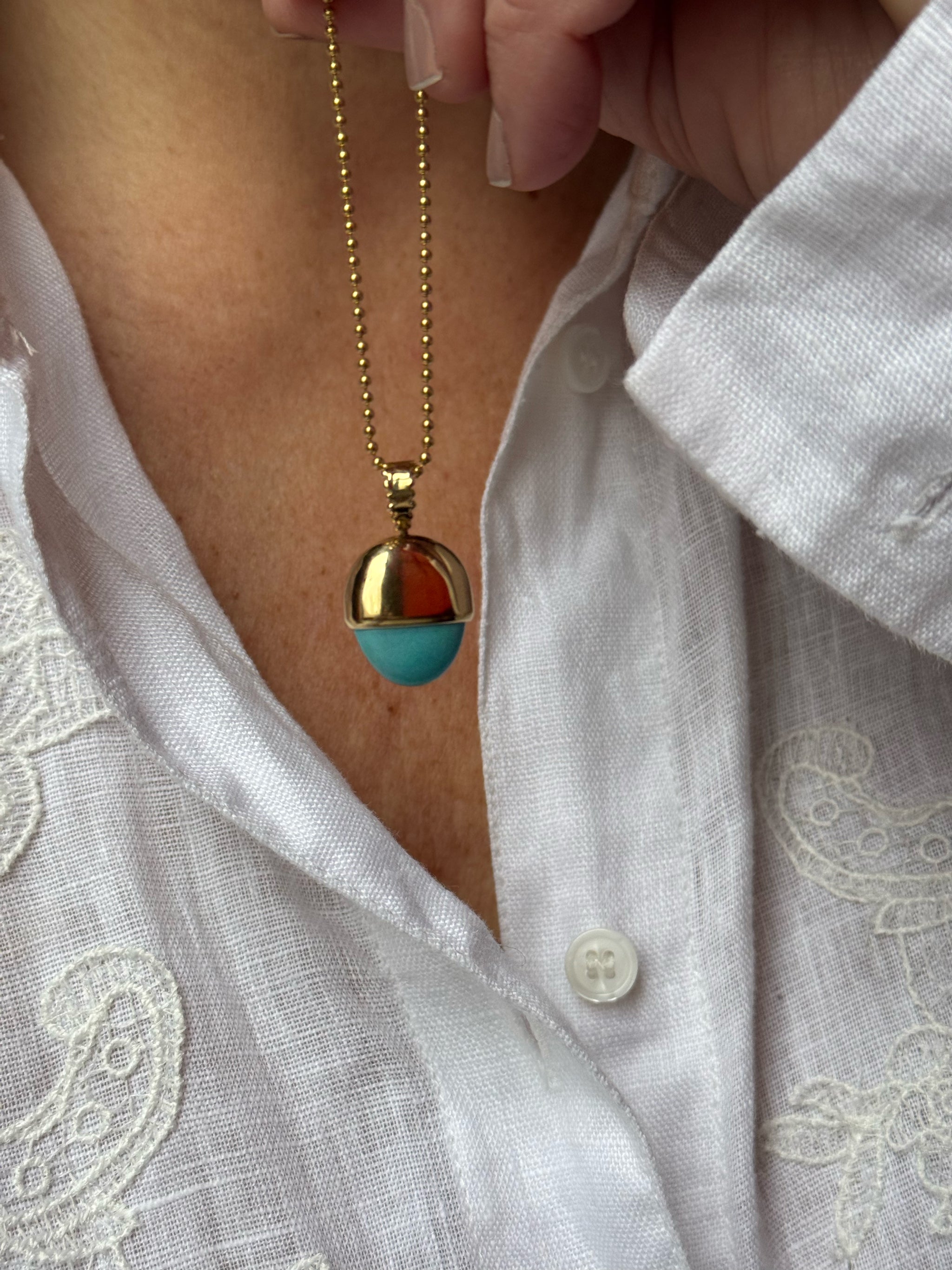 SeaSpell Le Pendule gold and turquoise pendulum necklace by Delphine Leymarie styled over white linen shirt, shown held for scale.
