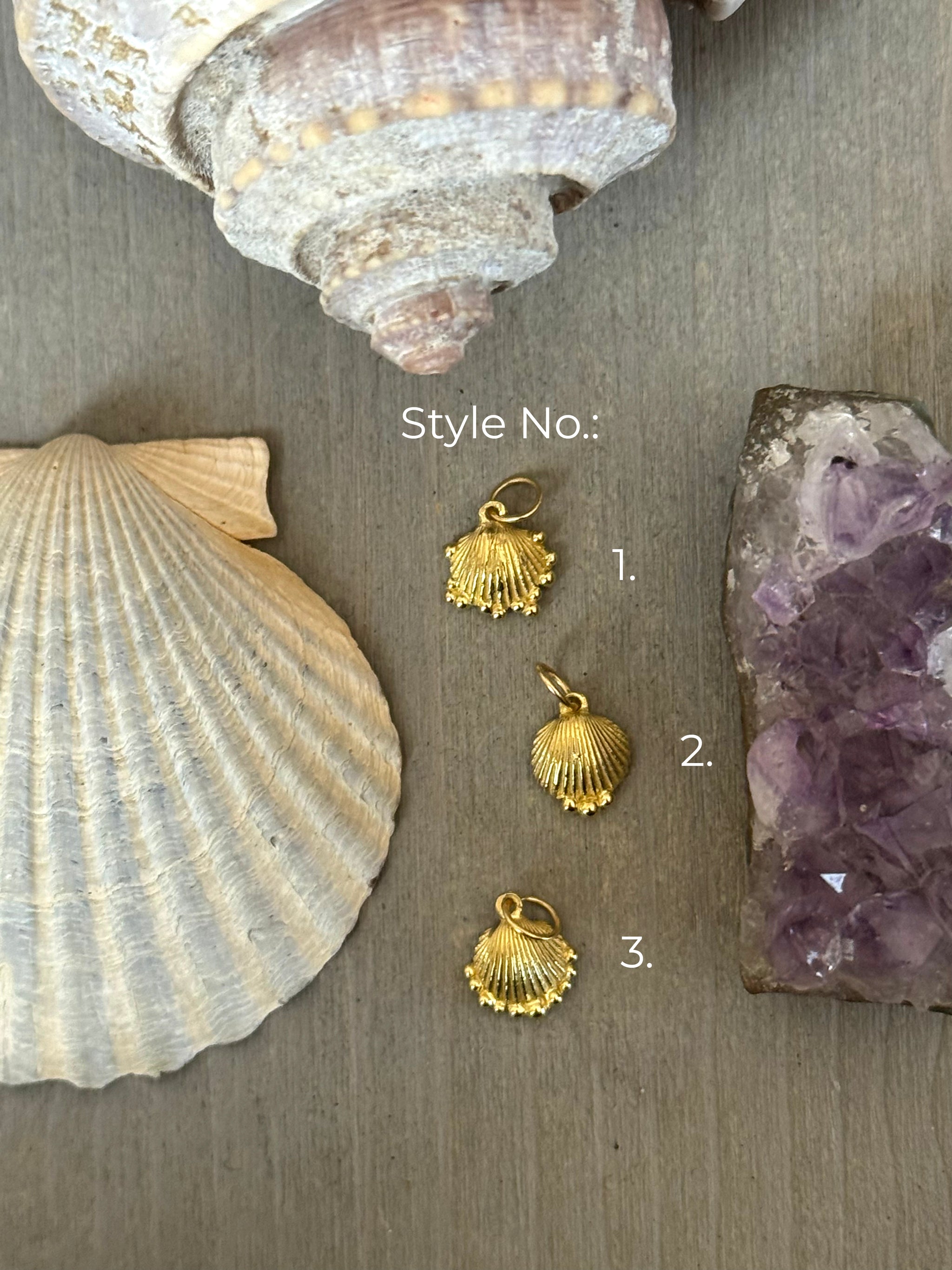 18k yeloow recycled gold shell-shaped talismans charms on a wooden surface with seashells and an amethyst crystal.