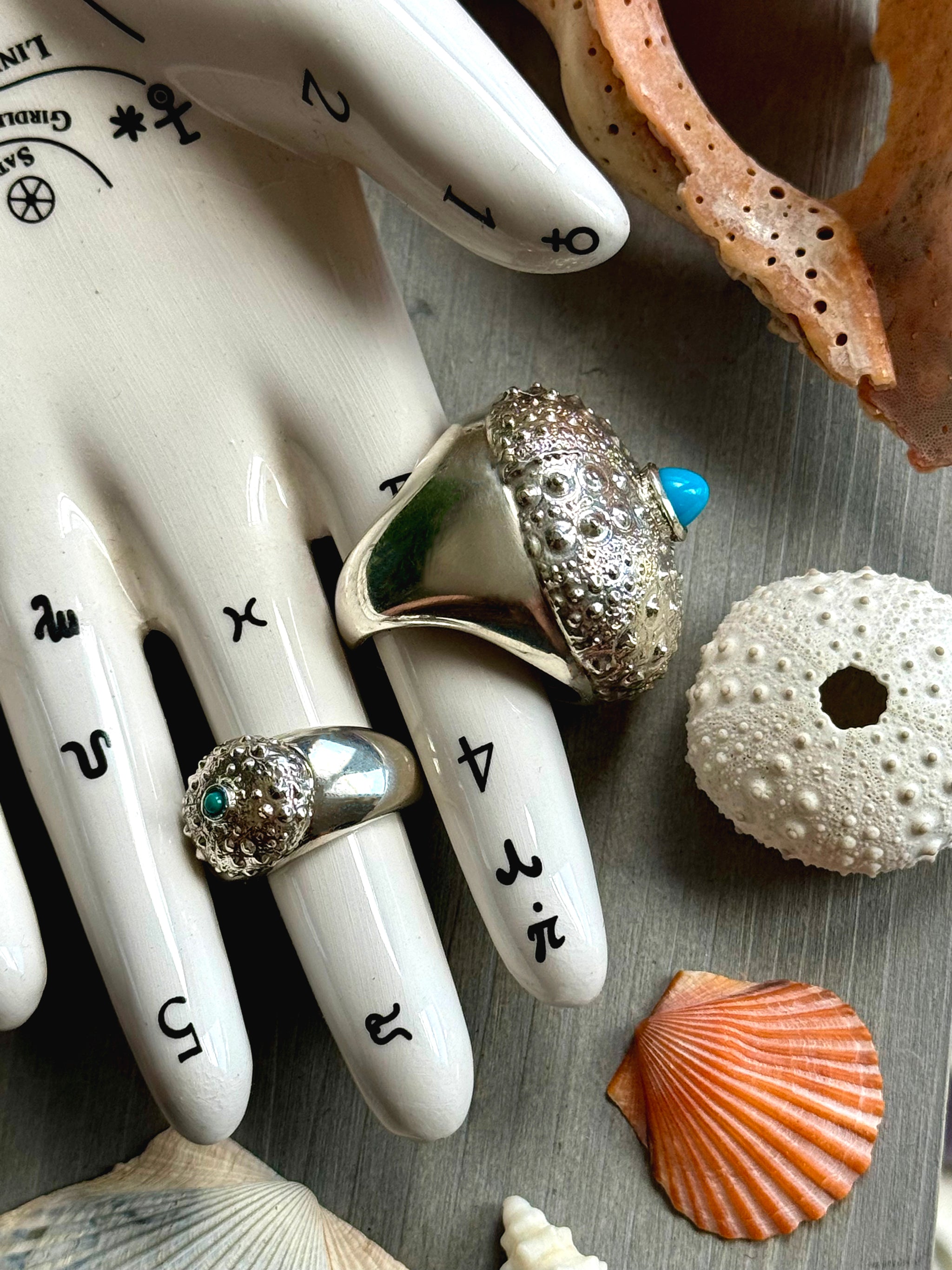Sideview of SeaSpell Grand Petit Urchin silver Ring on Tarot Hand over Grey Wood with Shells