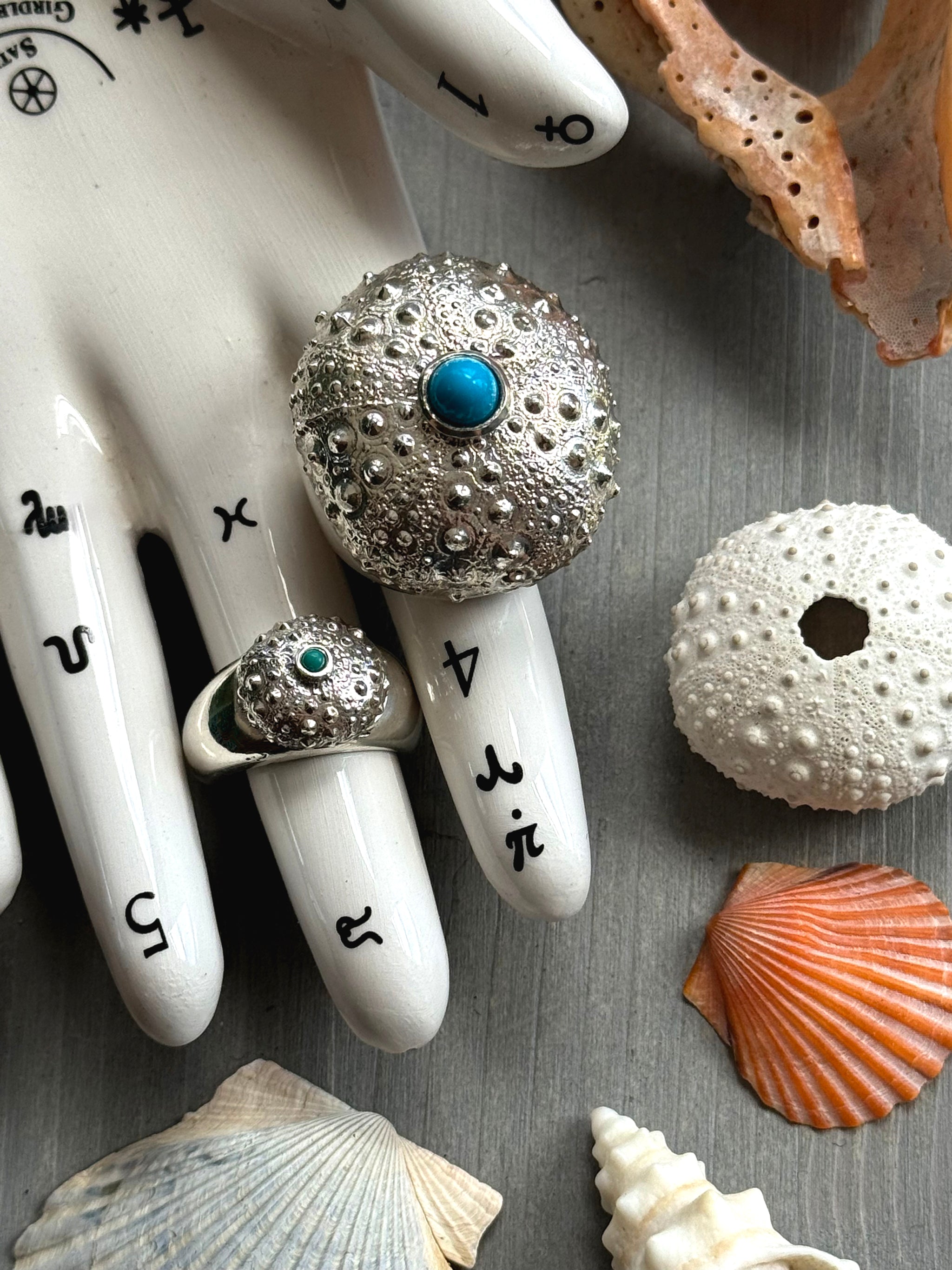 Top view of SeaSpell Grand Petit Urchin silver Ring on Tarot Hand over Grey Wood with Shells