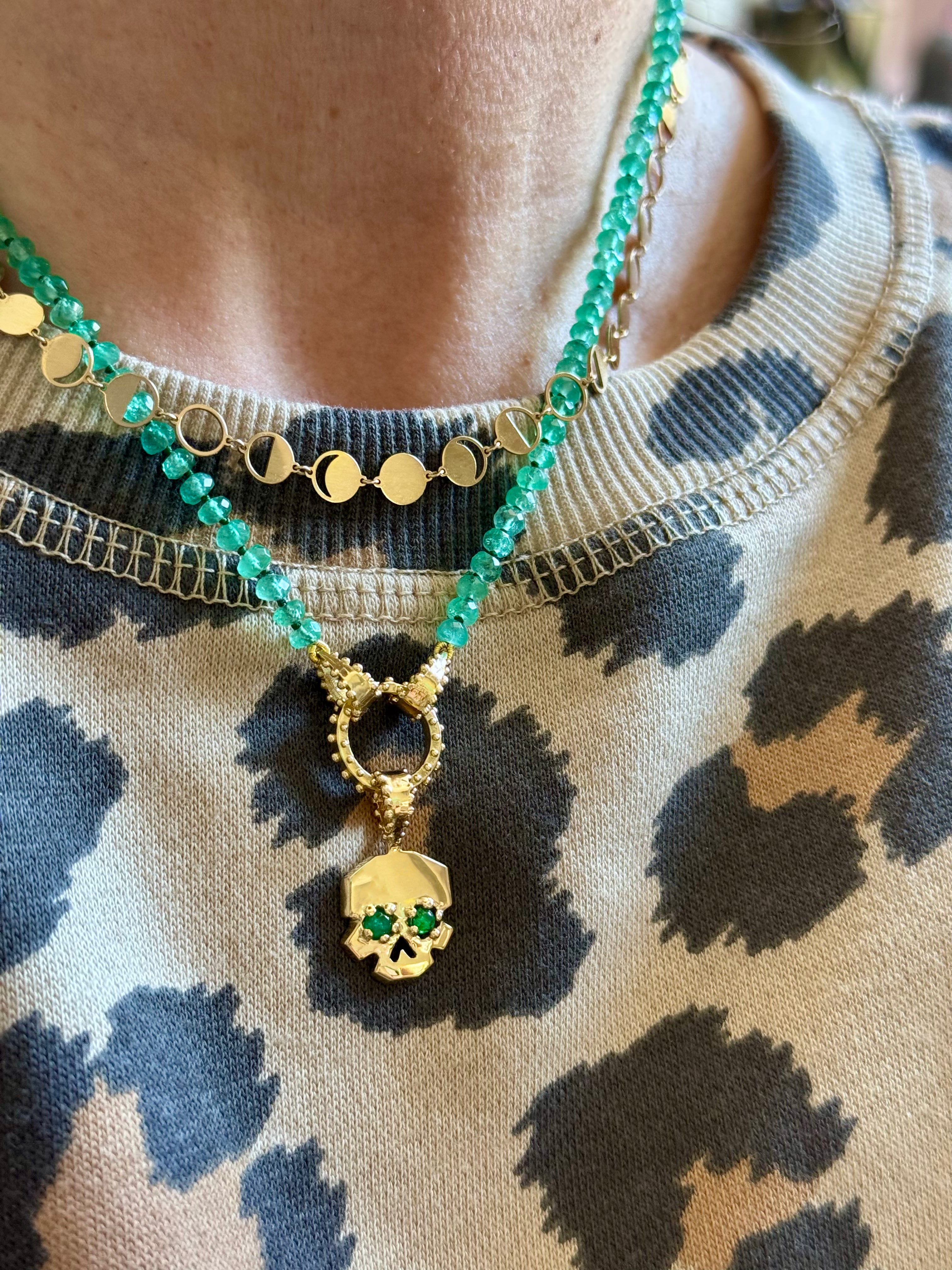 The Petite Lune gold chain necklace with circular cutouts featuring moon phases LayereD with THE FACETTE EMERALD EYE SKULL CHARM ON EMERALD CLICKER AND STRAND