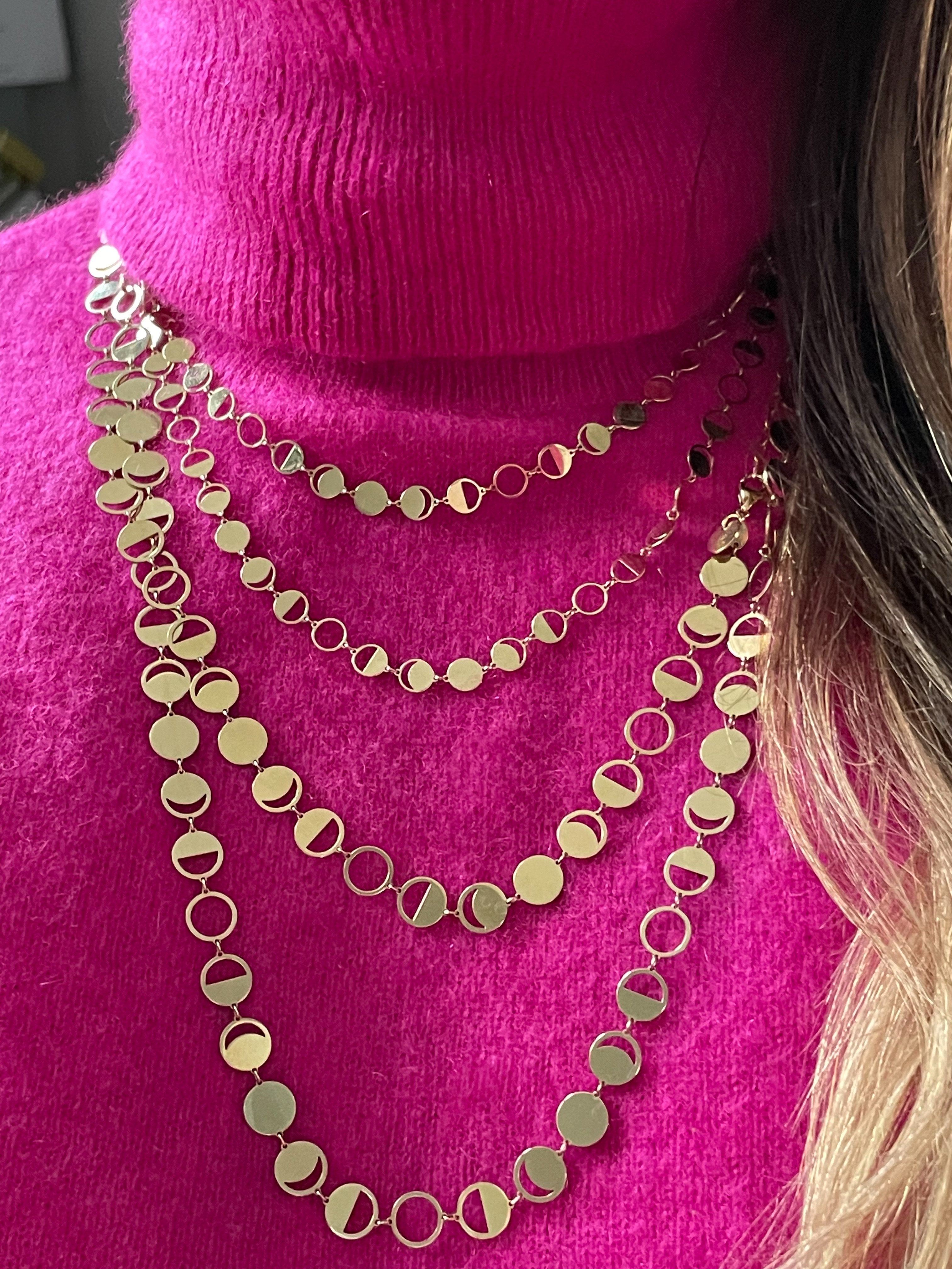 Solid 18k yellow gold Confetti Lune Petite and Regular diecut Moon Phase Chains layered on a Model's neck over pink cashemere turtleneck
