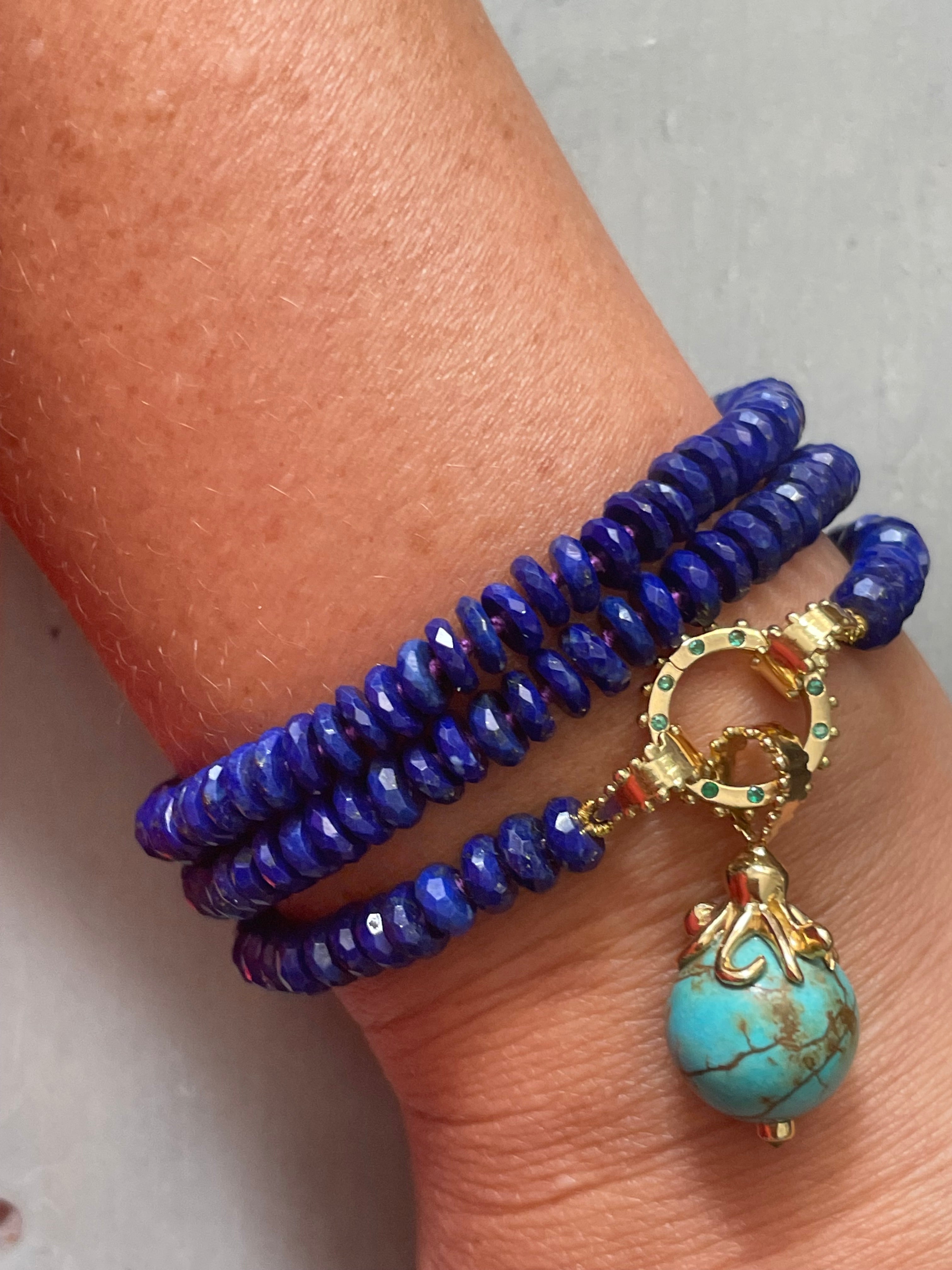 A strand of Delphine Leymarie deep blue lazuli beads on purple silk thread with gold beaded tear drop hoops at each end triple coiled on a wrist, closed with a Boheme Emerald Clicker holding the Turquoise Ocotpus charm