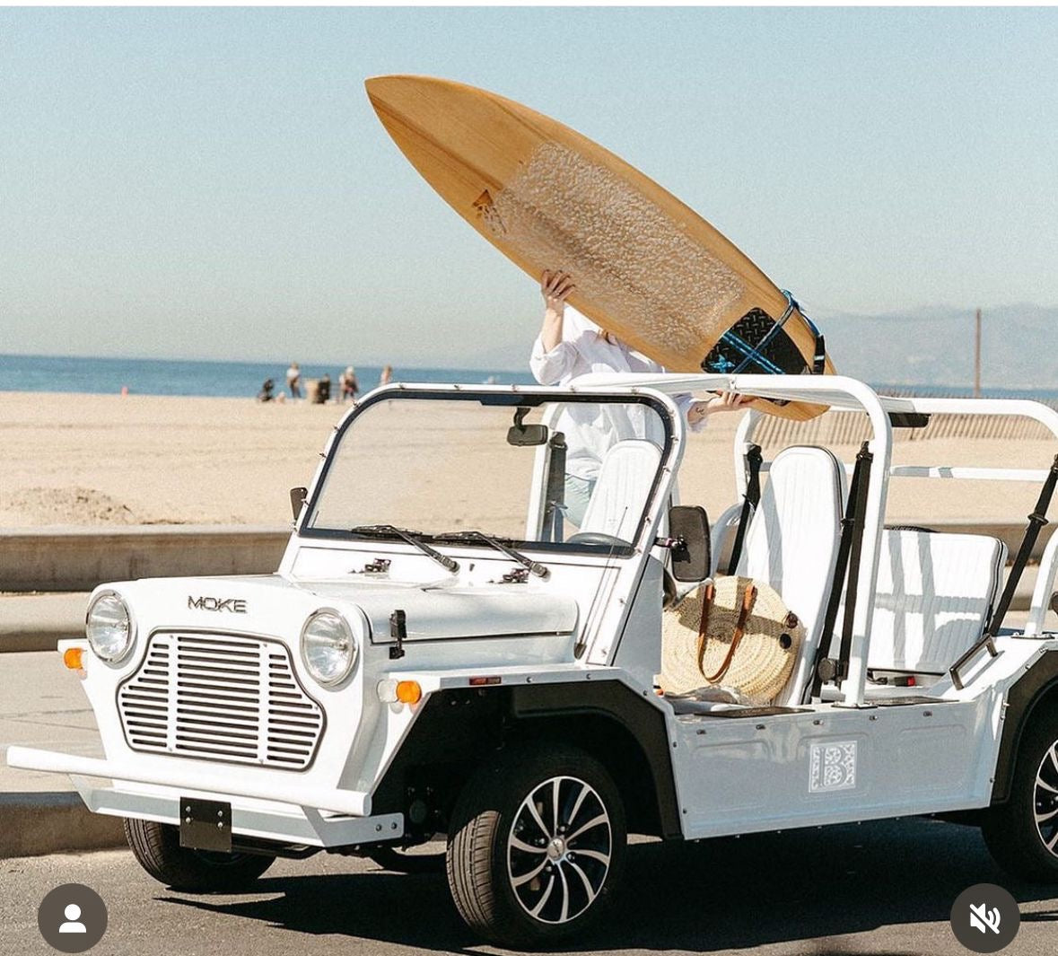 A surf bord being addde to a white jeep by a beach