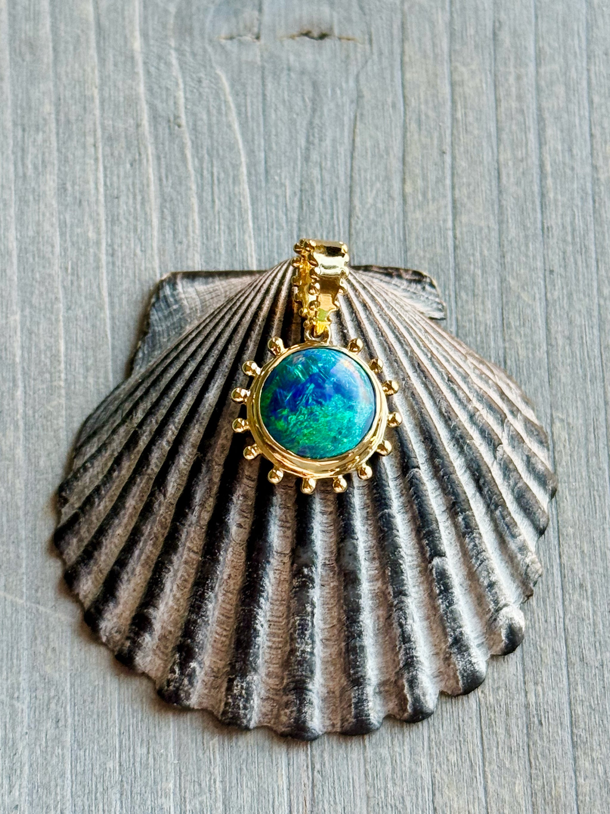Boheme Grand Soleil Charm with Australian blue green opal in 18k recycled gold on a grey seashell by Delphine Leymarie