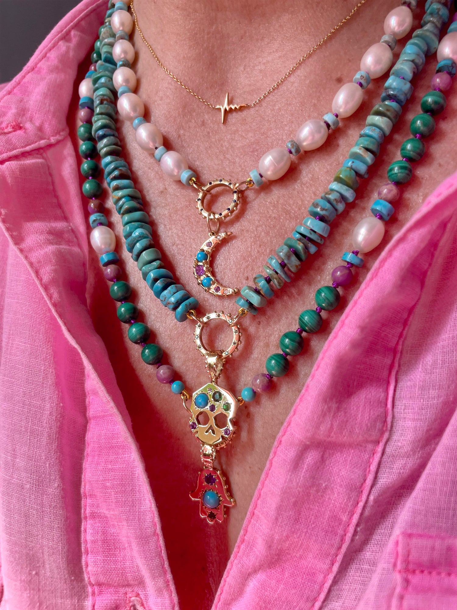 Close-up of a person wearing multiple necklaces with beads and gold pendants against a pink shirt.