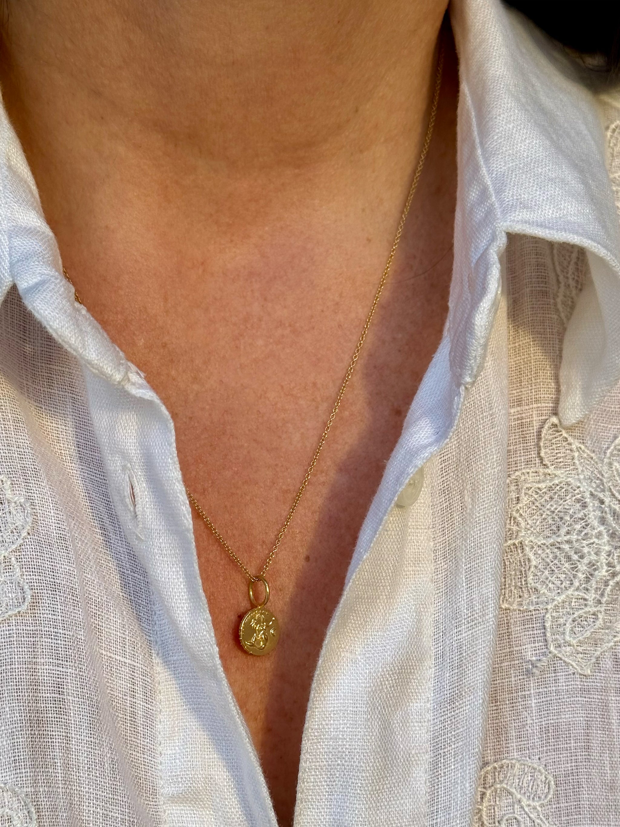 Close-up of solid 18k recycled gold tiny mermaid medallion Necklace worn with a white linen shirt with lace details.