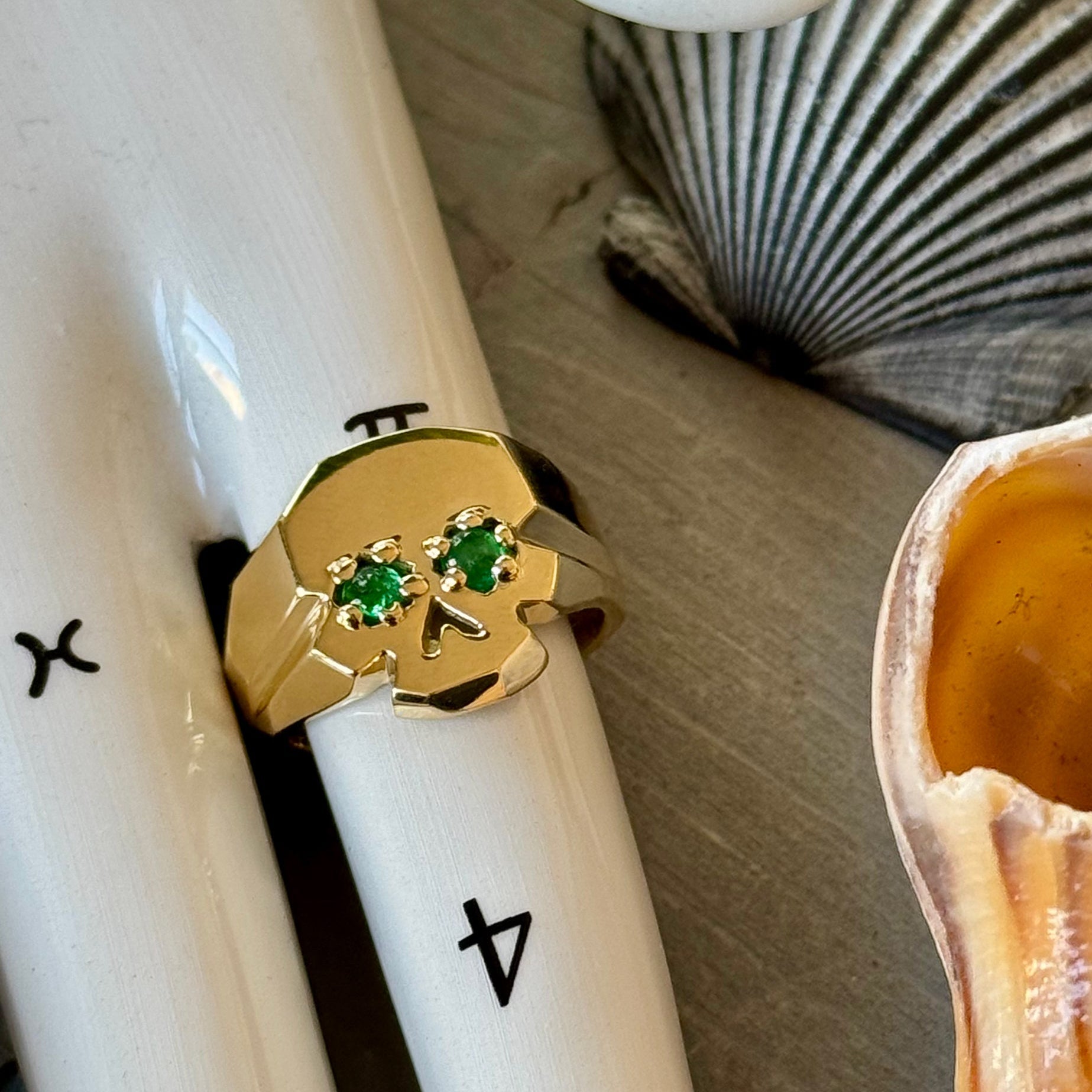 Facette Emerald Skull ring oin 18k yellow recycled giold on white porcelain Tarot hand surroudnde by seashells
