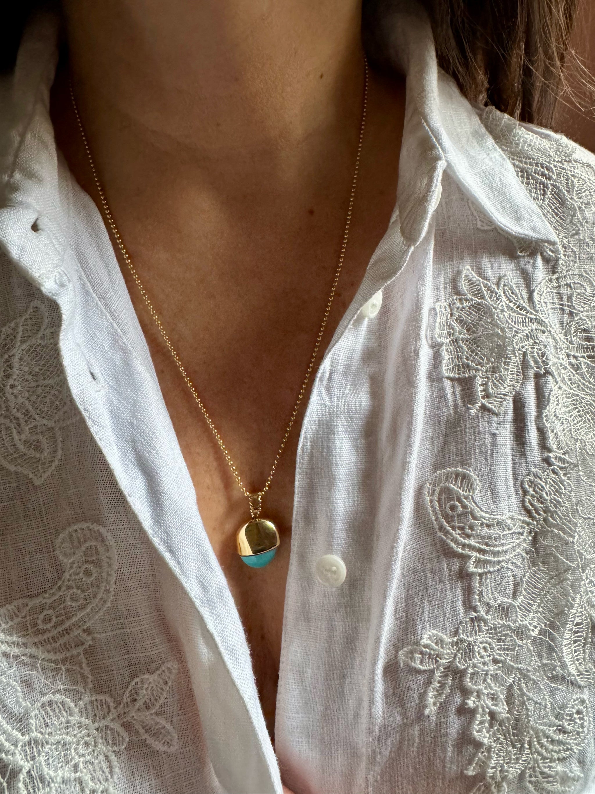 SeaSpell Le Pendule turquoise and 18k gold pendulum necklace by Delphine Leymarie worn on ball chain over white embroidered linen shirt.