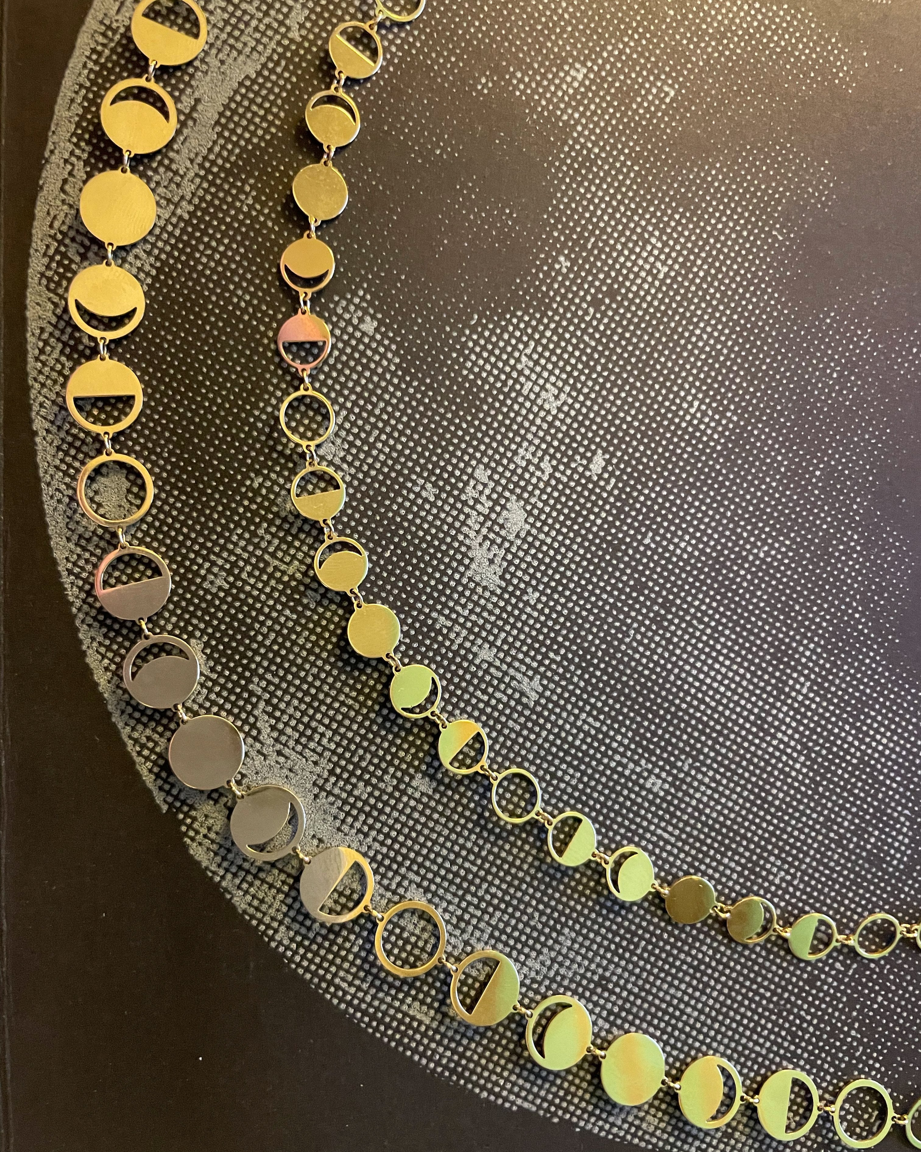 Solid 18k yellow gold Confetti Lune Petite and Regular diecut Moon Phase Chains over a picture of the moon.